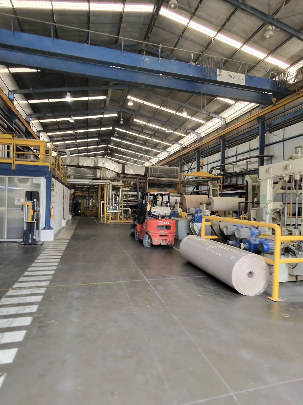 Paper mill production floor with a forklift and kraft reels beside the machine