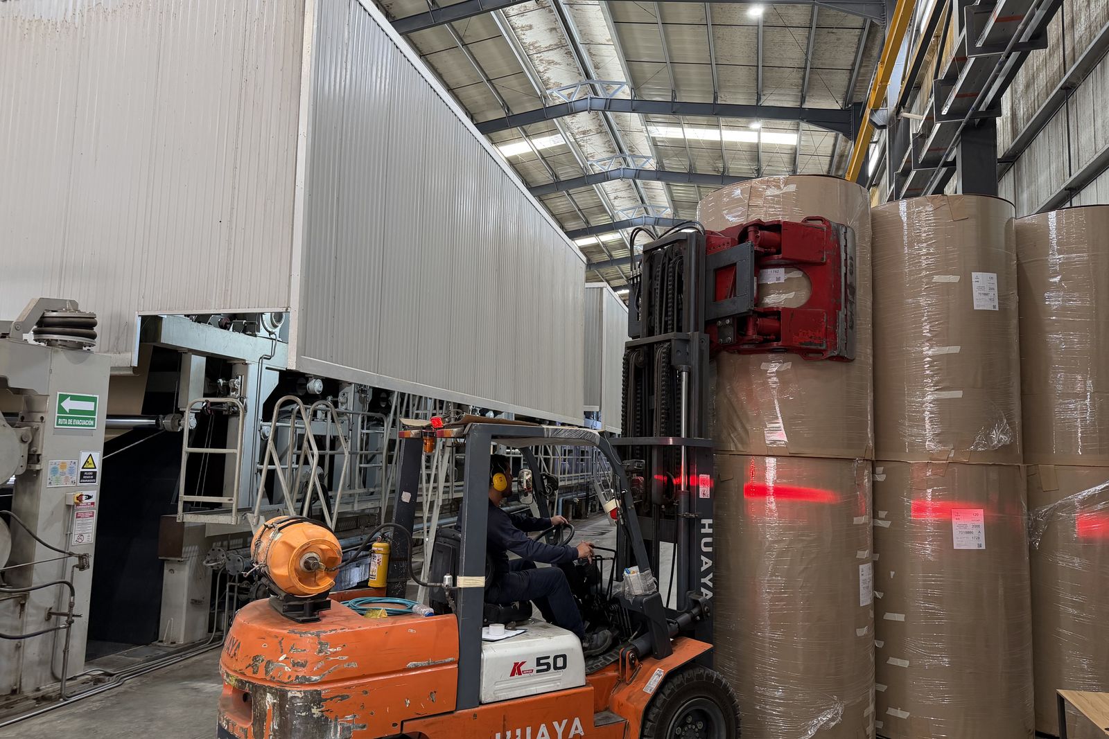 Clamp truck lifting a wrapped and labeled paper roll beside the machine at the Valle Kraft mill near Cali